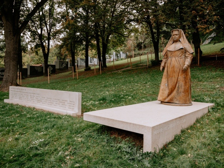 Pohled od betonových schodů k soše Marie Restituty a pamětní stěně v parku.