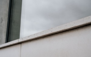 Sloup z pohledového betonu s jemnou strukturou u prosklené fasády polyfunkčního domu.