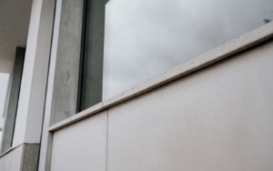Detail decentně strukturovaného parapetu z pohledového betonu pod prosklenou částí budovy.