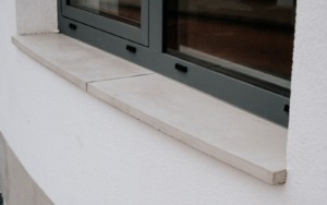 Detail parapetu z betonu v kombinaci s bílou omítkou budovy.