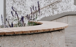 Detail betonového květináče s integrovanou dřevěnou lavičkou před polyfunkčním domem.