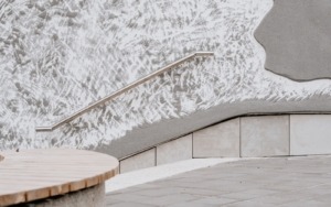 Detail nerezového zábradlí kotveného do dekorativní betonové fasády.