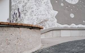 Detail zábradlí na šedobílé texturované betonové stěně u polyfunkčního domu.