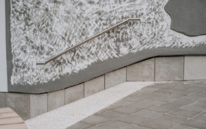 Ocelové zábradlí připevněné k reliéfní betonové fasádě budovy ve Šlapanicích.