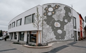 Boční pohled na polyfunkční dům ve Šlapanicích s výraznou betonovou uměleckou fasádou.