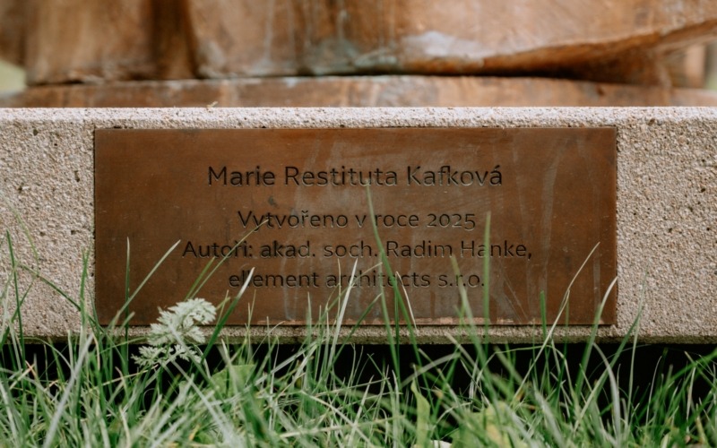 Bronzová informační tabulka k soše Marie Restituty instalované na betonovém podstavci.