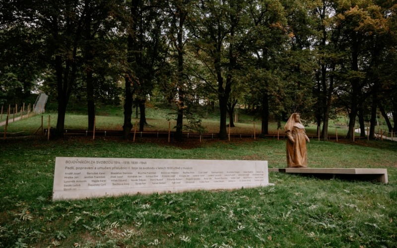 Betonová pamětní stěna s vyrytými jmény a socha Marie Restituty v parku v Brně.