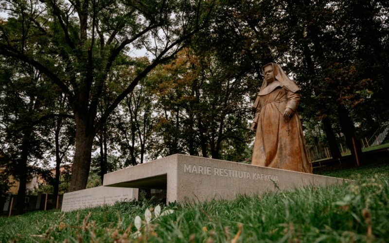 Pohled od betonových schodů k soše Marie Restituty a pamětní stěně v parku.