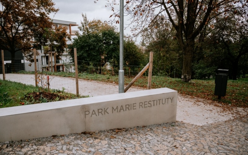 Betonová vstupní stěna s nápisem Park Marie Restituty u chodníku.