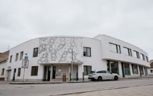 Polyfunkční dům ve Šlapanicích s dekorativní fasádou a betonovými prvky u vstupu.