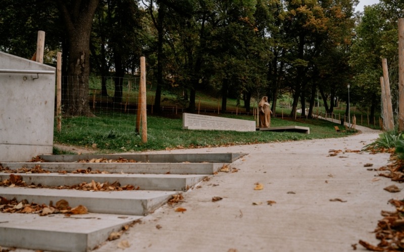 Chodník kolem sochy Marie Restituty s betonovým podstavcem a pamětní stěnou.