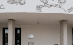 Vstupní prostor polyfunkčního domu s betonovými sloupy a moderní fasádou.